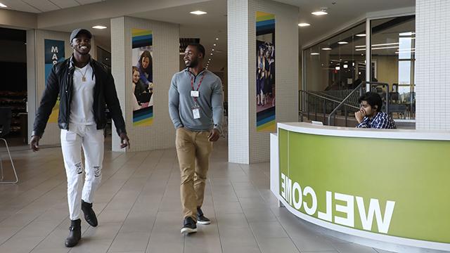 a 赌钱app可以微信提现 staff member walks with a student in the Student Center near the Welcome desk